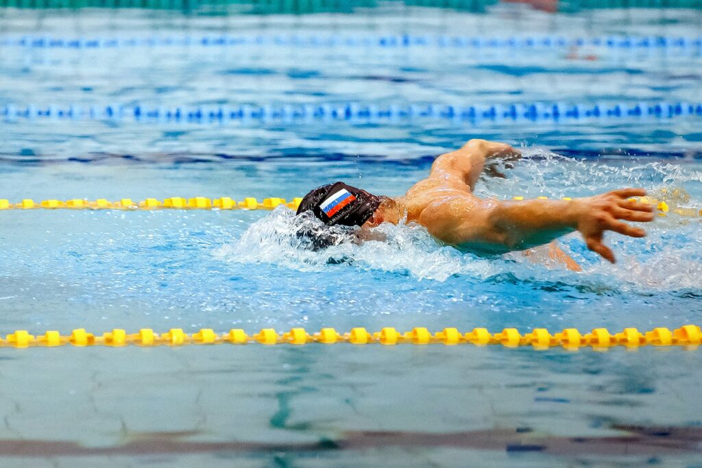 male athlete swim butterfly race in swimming competition, flag russian team is swimmer cap